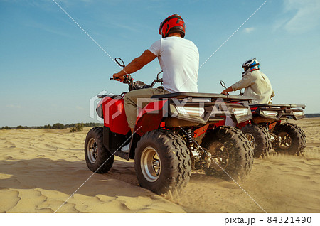Two men in helmets riding on atv in desert sands 84321490