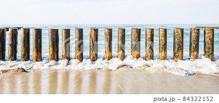 Wooden breakwater on the sandy shore, washed by the waves against the background of the sea 84322152