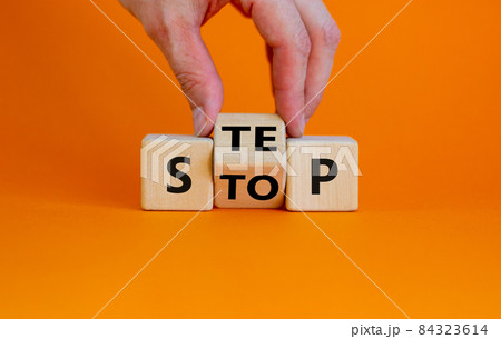 Stop or next step symbol. Businessman turns cubes and changes the word 'stop' to 'step'. Beautiful orange background, copy space. Business, stop or next step concept. Stop or next step symbol. Businessman turns cubes and changes the word 'stop' to 'step'. Beautiful orange background, copy space. Business, stop or next step concept. 84323614