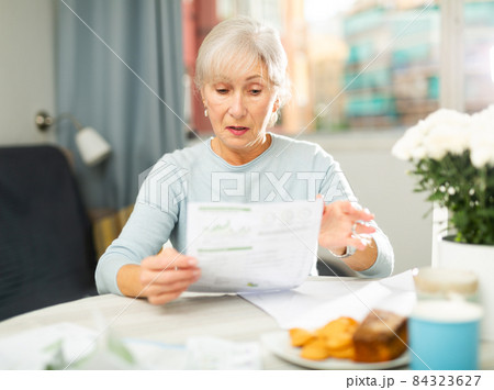 Senior woman reading papers with interest at home table 84323627
