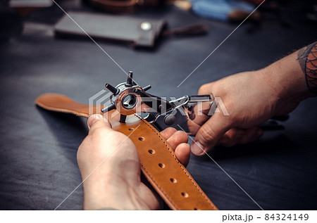 Craftsman performs leather working for a new product in his tanning shop 84324149