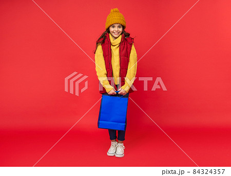 happy kid in winter hat hold shopping bags on red background, shopping happy kid in winter hat hold shopping bags on red background, shopping 84324357
