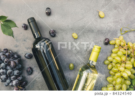Top view of bottle red and white wine, green vine, wineglass and ripe grape on vintage dark stone table background. Wine shop wine bar winery or wine tasting concept Top view of bottle red and white wine, green vine, wineglass and ripe grape on vintage dark stone table background. Wine shop wine bar winery or wine tasting concept 84324540