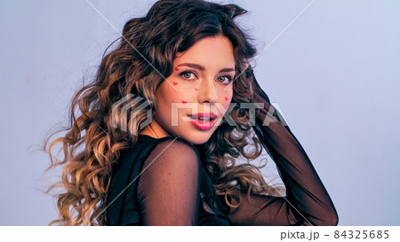 Beautiful model with drawn hearts on her cheeks posing in the studio. A fashion model touching her hair is photographed in a photo studio looking at the camera. Beautiful young woman with long hair.. 84325685