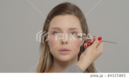 Applying mascara to the lashes. Make-up artist in beauty studio doing makeup for beautiful girl. Woman making up using comb for eyelashes. Young woman making makeup in dressing makeup room. Making 84325865