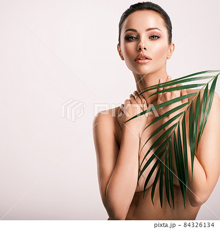 Young beautiful woman with green leaves near naked body. Body care beauty treatments concept.  Girl's  face with green flowers. 84326134