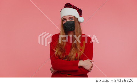 Woman in Christmas red sweater wearing face mask ppe to safe from coronavirus on lockdown quarantine Woman in Christmas red sweater wearing face mask ppe to safe from coronavirus on lockdown quarantine 84326820