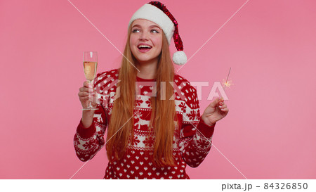 Lovely girl in Christmas Santa sweater dancing with bengal sparklers fireworks and champagne glass Lovely girl in Christmas Santa sweater dancing with bengal sparklers fireworks and champagne glass 84326850
