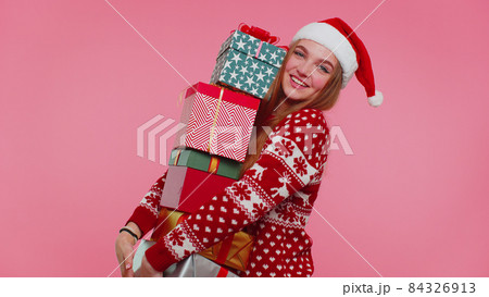 Woman in Christmas red sweater, Santa hat smiling holding many gift boxes New Year presents shopping 84326913