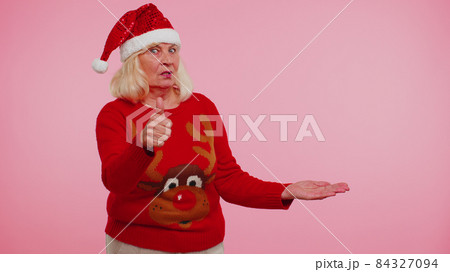 Grandmother in Christmas deer sweater showing thumbs up and pointing at on blank advertisement space Grandmother in Christmas deer sweater showing thumbs up and pointing at on blank advertisement space 84327094