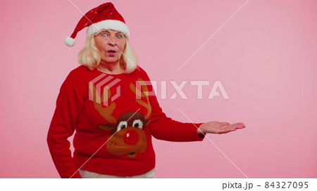Grandmother in Christmas deer sweater showing thumbs up and pointing at on blank advertisement space Grandmother in Christmas deer sweater showing thumbs up and pointing at on blank advertisement space 84327095