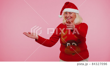 Grandmother in Santa Christmas sweater showing thumbs up and pointing empty place, advertising area Grandmother in Santa Christmas sweater showing thumbs up and pointing empty place, advertising area 84327096