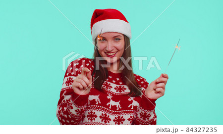 Lovely girl in Christmas Santa sweater dancing with bengal sparklers fireworks ligts, congratulation Lovely girl in Christmas Santa sweater dancing with bengal sparklers fireworks ligts, congratulation 84327235