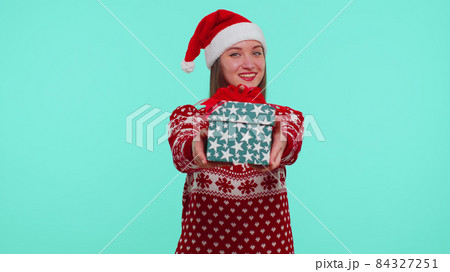Joyful girl in red Christmas sweater with deers presenting Christmas gift box, shopping holiday sale 84327251