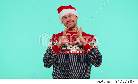 Smiling man in Christmas sweater makes heart gesture demonstrates love sign expresses good feelings Smiling man in Christmas sweater makes heart gesture demonstrates love sign expresses good feelings 84327887