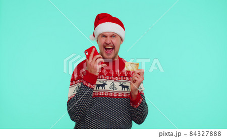 Man in Christmas red sweater use mobile cell phone and plastic credit bank card, win, calebrate, wow Man in Christmas red sweater use mobile cell phone and plastic credit bank card, win, calebrate, wow 84327888