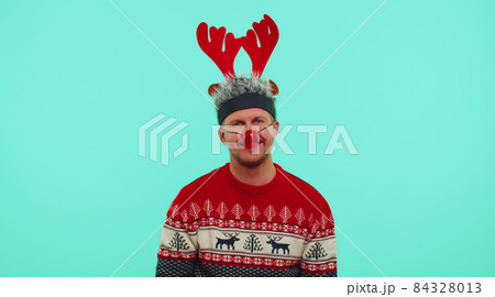 Cheerful lovely 30s years old man wears red New Year sweater and hat smiling, looking at camera Cheerful lovely 30s years old man wears red New Year sweater and hat smiling, looking at camera 84328013