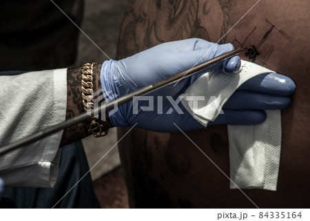 Tattooing concepts. The artist is tattooing a Thai style pattern on the skin with a pointed metal. 84335164
