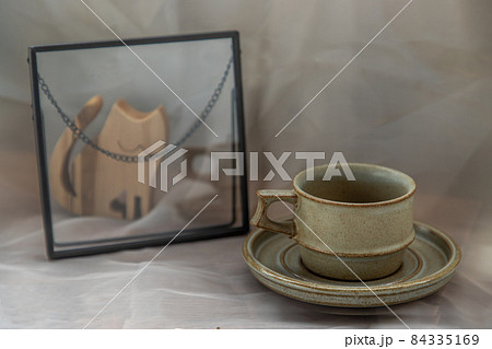 Handmade ceramic coffee mug with wooden doll in cat shape on fabric textured table cloth. 84335169