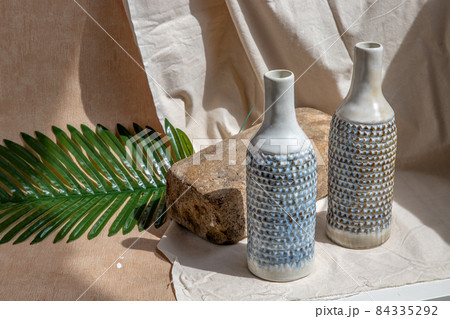 Two white and blue handmade ceramic vases on white textured table cloth. 84335292