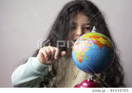 Little girl portrait holding a globe in hand and spin it by right hand Little girl portrait holding a globe in hand and spin it by right hand 84339765