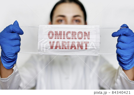 Female doctor holds a face mask with - Omicron variant text on it. Covid-19 new variant - Omicron. Omicron variant of coronavirus. SARS-CoV-2 variant of concern Female doctor holds a face mask with - Omicron variant text on it. Covid-19 new variant - Omicron. Omicron variant of coronavirus. SARS-CoV-2 variant of concern 84340421