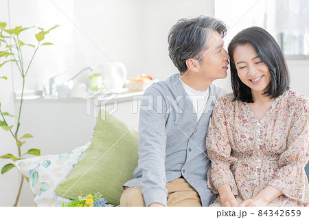 リビングのソファに座って耳元で囁くミドルエイジの男性と女性のカップル リビングのソファに座って耳元で囁くミドルエイジの男性と女性のカップル 84342659