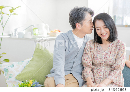 リビングのソファに座って耳元で囁くミドルエイジの男性と女性のカップル リビングのソファに座って耳元で囁くミドルエイジの男性と女性のカップル 84342663
