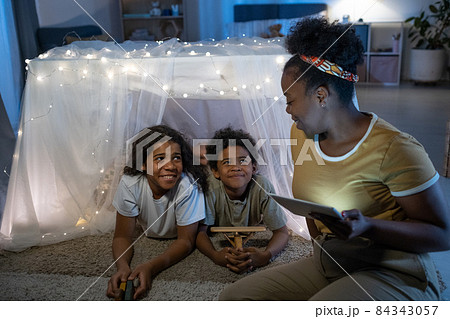Smiling blackwoman using tablet while reading online book to children inside of play tent before bed Smiling blackwoman using tablet while reading online book to children inside of play tent before bed 84343057