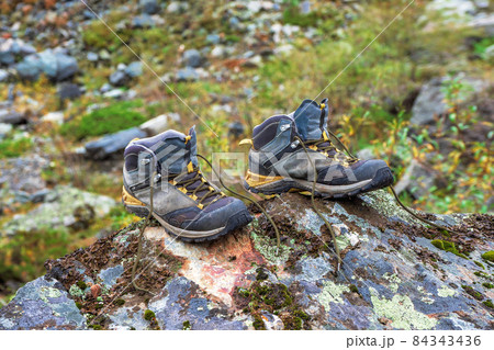 Hiking boots on drying. Wet hiking boots dry on a stone against the background of snow-covered high mountains. The difficulties of hiking, drying clothes in nature. Hiking boots on drying. Wet hiking boots dry on a stone against the background of snow-covered high mountains. The difficulties of hiking, drying clothes in nature. 84343436
