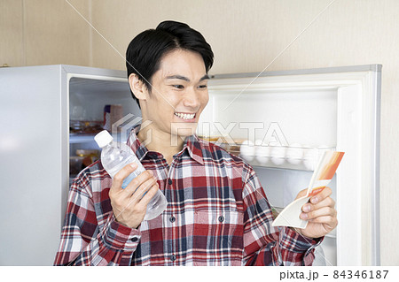 冷蔵庫を開けたまま預金通帳を見て微笑む男性 84346187