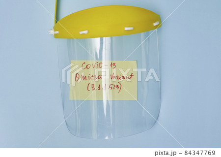 Covid plastic face shield and memo note with text Omicron variant of covid-19 virus. 84347769