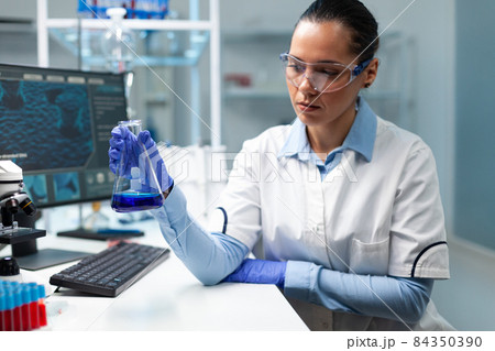Biologist researcher holding transparent glassware analyzing blue solution 84350390