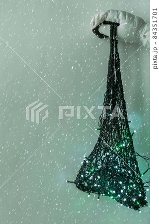 A string bag with a burning garland in hand with a white mitten in a snowfall. 84351701