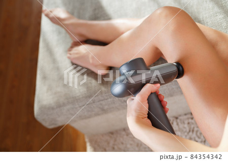 A woman massages her legs with an automatic pistol at home. A woman massages her legs with an automatic pistol at home. 84354342