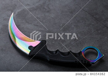 Kerambit dagger with a rainbow-colored blade on a dark textured background. 84354362