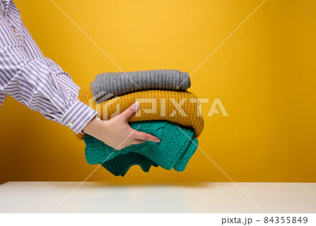woman holding a stack of knitted folded sweaters on a yellow background. Washing clothes, cleaning things woman holding a stack of knitted folded sweaters on a yellow background. Washing clothes, cleaning things 84355849