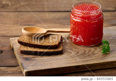 full glass jar with red caviar on a brown wooden table 84355865
