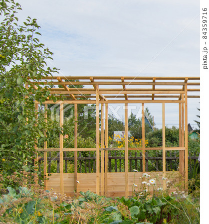 Wooden frame construction of a new veranda or gazebo on the territory of a country plot, in summer, outdoors Wooden frame construction of a new veranda or gazebo on the territory of a country plot, in summer, outdoors 84359716