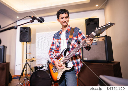 a male guitarist plays an electric guitar with a band in the background a male guitarist plays an electric guitar with a band in the background 84361190