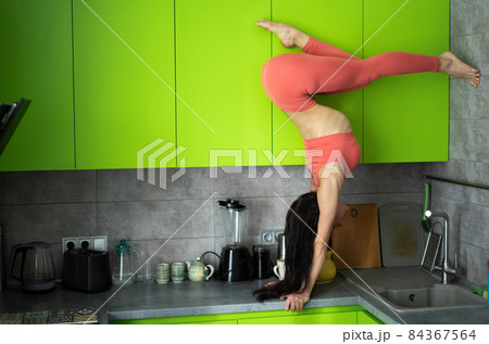 Woman on the kitchen doing exercise and handstand. Concept of individuality, creativity and self-confidence Woman on the kitchen doing exercise and handstand. Concept of individuality, creativity and self-confidence 84367564