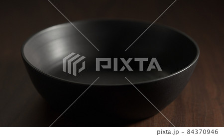 Black ceramic bowl on walnut wood table closeup Black ceramic bowl on walnut wood table closeup 84370946