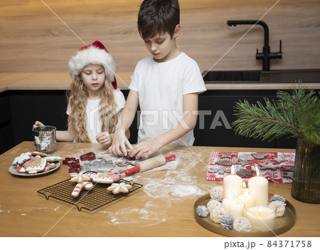 Children - a boy and a girl are preparing gingerbread in the kitchen Children - a boy and a girl are preparing gingerbread in the kitchen 84371758