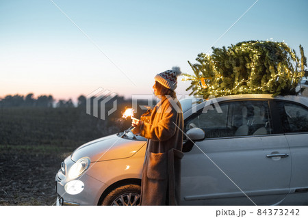Woman with sprklers near car and Christmas tree outdoors Woman with sprklers near car and Christmas tree outdoors 84373242