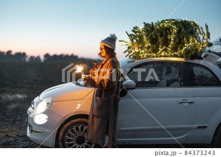 Woman with sprklers near car and Christmas tree outdoors Woman with sprklers near car and Christmas tree outdoors 84373243