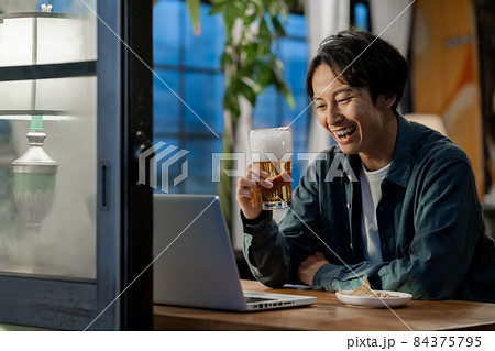 夜ビールを飲みながらzoomで話をする若い男性 84375795