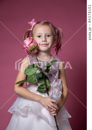 Little caucasian girl in a festive dress with sequins posing with rose flower Little caucasian girl in a festive dress with sequins posing with rose flower 84378101