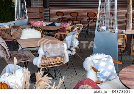 Empty tables and chairs with cushions, fur warm covers, wicker furniture and gas heaters Empty tables and chairs with cushions, fur warm covers, wicker furniture and gas heaters 84378655