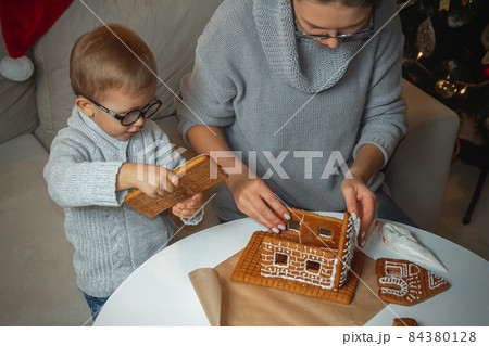 Little boy with mom decorate christmas gingerbread house together Little boy with mom decorate christmas gingerbread house together 84380128