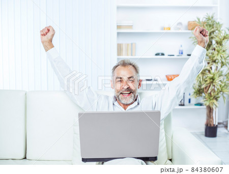 enthusiastic businessman with an open laptop sitting on sofa in modern office. 84380607